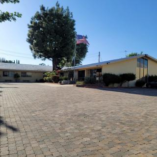 A one-story building with an American flag and a large tree, set in a sunny, clear-sky day.