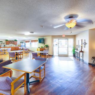 A spacious, well-lit community room with tables, chairs, and a ceiling fan.