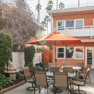 A cozy outdoor patio area with a table, chairs, and an orange umbrella in front of a two-story house.