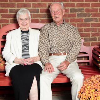 An elderly couple sitting together on a bench in front of a brick wall.