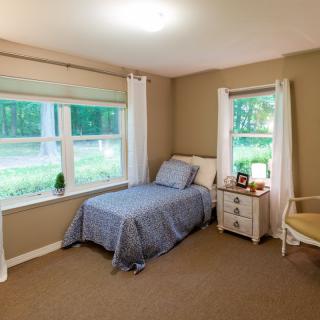A cozy bedroom with a single bed and large windows overlooking a wooded area.