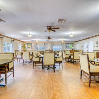 A spacious dining area with neatly arranged chairs and tables, ceiling fans, and ample natural lighting.