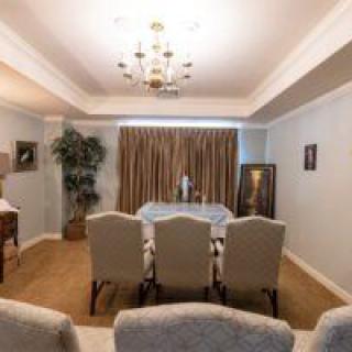 A well-furnished dining room featuring a large table with six chairs, a chandelier, and elegant curtains.