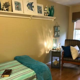 A cozy bedroom with a bed, chair, and decorative elements like artwork and a lamp.