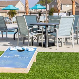 A relaxing poolside setup with patio furniture and a cornhole game on the lawn.