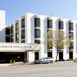 A view of a hospital and medical center building with a parking area in front.