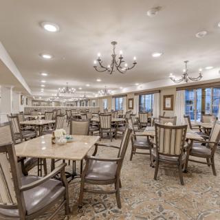 A spacious dining room with neatly arranged tables and chairs, illuminated by elegant chandeliers.