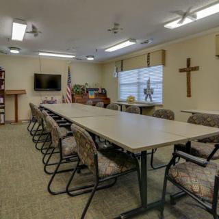 A conference room with a long table surrounded by chairs, featuring a cross on the wall and an American flag in the corner.