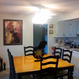 A cozy dining area with a wooden table and chairs, decorated with artwork on the wall, adjacent to a kitchen.
