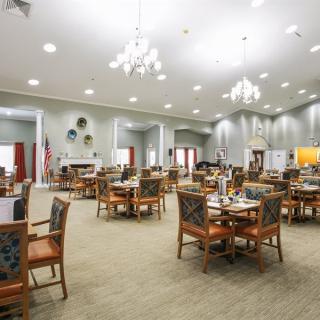 A spacious and well-lit dining area with multiple tables and chairs, featuring elegant chandeliers.