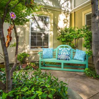 A tranquil garden setting with a turquoise bench adorned with colorful cushions surrounded by lush greenery.