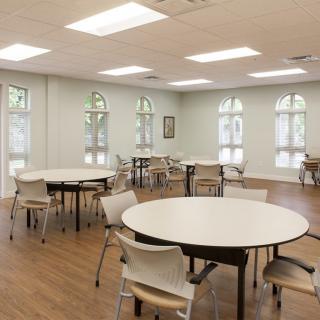 An empty classroom with round tables and chairs under bright fluorescent lights.