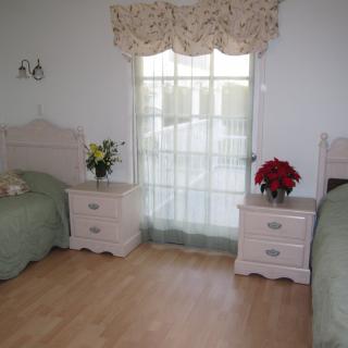 A cozy bedroom with twin beds, floral decorations, and a window with sheer curtains.