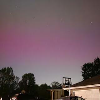 A mesmerizing display of purple hues in the night sky, captured from a backyard with a basketball hoop.