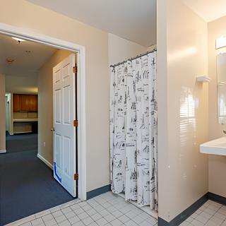 A clean bathroom with a shower curtain, sink, and doorway leading to a hallway.