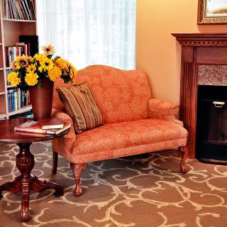 A cozy living room with an orange sofa, a wooden table with flowers, and a fireplace.