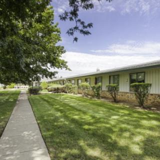 A suburban residential area with a pathway leading past a single-story building and well-maintained lawns under a clear sky.