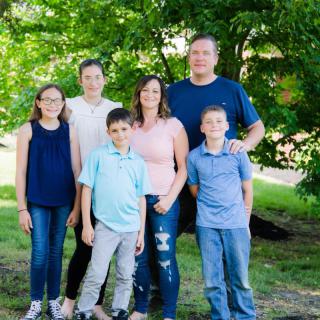 A family of six posing together in a lush green park.
