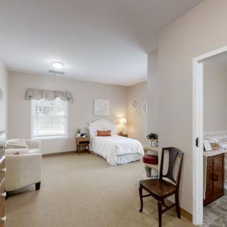 A cozy bedroom with a neatly made bed, a chair, and a window letting in natural light.