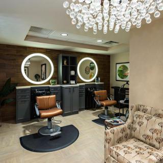 A modern salon interior featuring stylish barber chairs, illuminated mirrors, and a decorative chandelier.