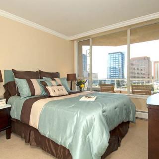 A modern bedroom with elegant decor and a large window offering a city view.