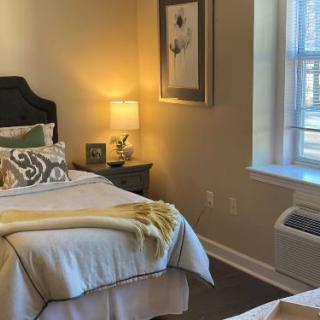 A cozy bedroom with a neatly made bed, decorative pillows, and a warm lamp on the nightstand.
