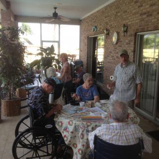 A group of seniors gathered around a table on a porch, enjoying conversation.