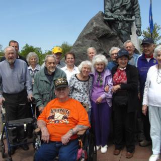 A group of elderly people gathered outdoors near a monument.