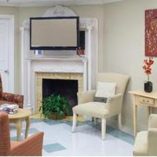 A cozy living room with a television above the fireplace, surrounded by comfortable chairs and tasteful decor.