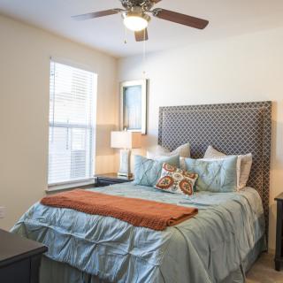 A cozy bedroom featuring a neatly made bed with decorative pillows, a bedside lamp, and natural light streaming through the window.