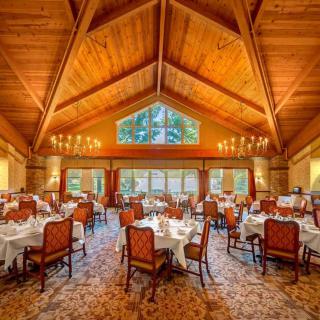 An elegant dining room with a wooden ceiling and chandeliers, set up for a fine dining experience.