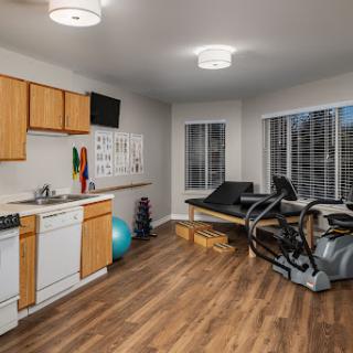 A modern home gym featuring exercise equipment and a kitchen area, illuminated by natural light.