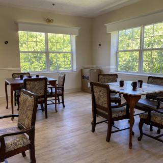 A bright dining area with multiple tables and chairs, illuminated by natural light from large windows.