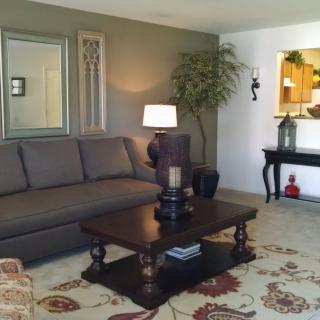 A cozy living room featuring a large sofa, elegant coffee table, and decorative elements including a mirror and indoor plant.