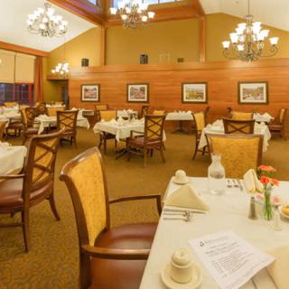 An elegant dining room with neatly arranged tables and chairs, illuminated by chandeliers.