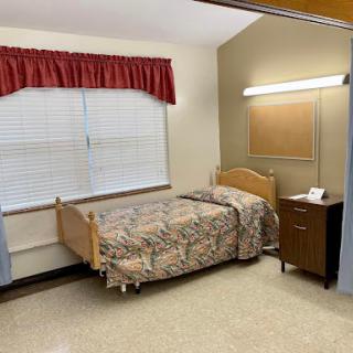 A simple hospital room featuring a single bed, bedside table, and window.