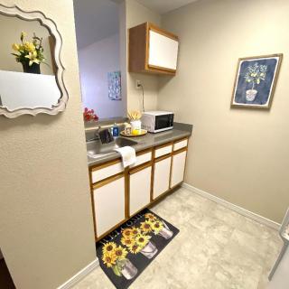 A small, decorated kitchen area with a microwave, cabinets, and a sunflower-themed rug.