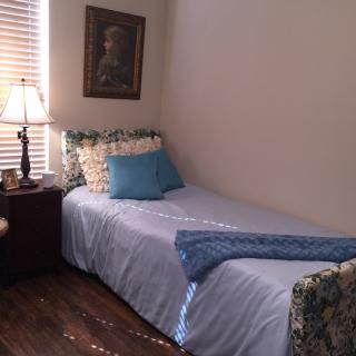 A cozy bedroom with a single bed and decorative pillows beside a nightstand and lamp.