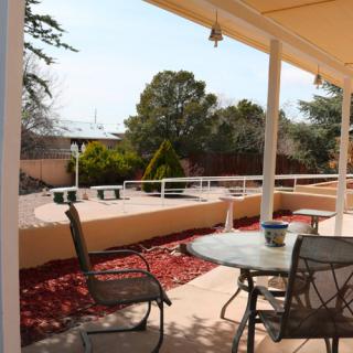 A sunny outdoor patio with a table and chairs, overlooking a landscaped backyard with trees.