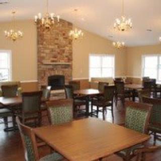 A cozy dining room with wooden tables and chairs, featuring a central fireplace and elegant chandeliers.