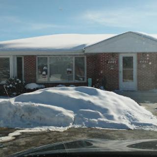 A cozy house partially covered in snow on a sunny winter day.