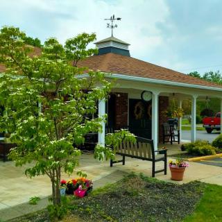 A charming building with a porch and weather vane, surrounded by a garden with flowers and a tree.
