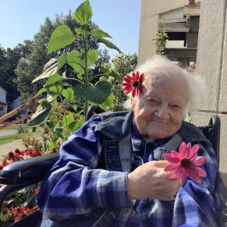 An elderly woman enjoying the beauty of flowers in her garden while sitting in a wheelchair.