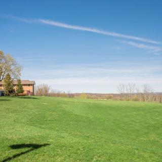 A scenic view of a house on a grassy field under a clear blue sky.