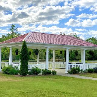 A picturesque white gazebo set amidst a green park with a cloudy sky overhead.