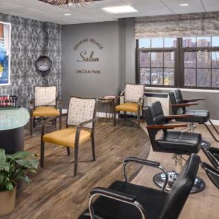A modern hair salon with a stylish interior, featuring comfortable chairs, large windows, and decorative elements.