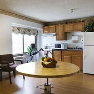 A cozy kitchen and dining area with a round table and chairs, featuring wooden cabinets, a refrigerator, and a microwave under a large window.