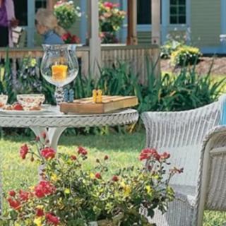 A charming garden patio featuring wicker furniture, a table set with drinks, and vibrant flowers.