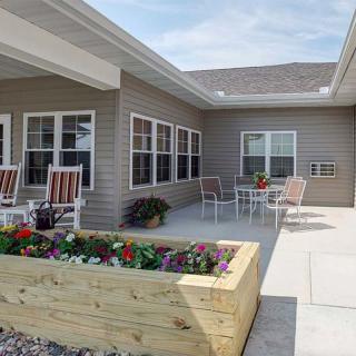 A cozy patio area featuring outdoor seating and a wooden flower bed, set against the exterior of a building.