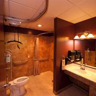 An accessible bathroom with modern amenities, featuring a toilet, sink, mirror, and handrails for support.